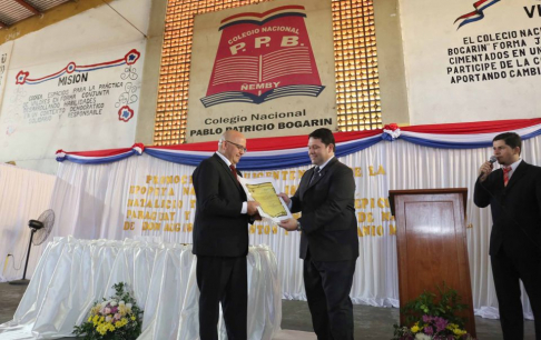 Preciso instante en el que el Dr. Miguel Angel Pereira entrega el reconocimiento al Lic. Tomas Olmedo, director del Colegio Nacional Pablo Patricio Bogarín.